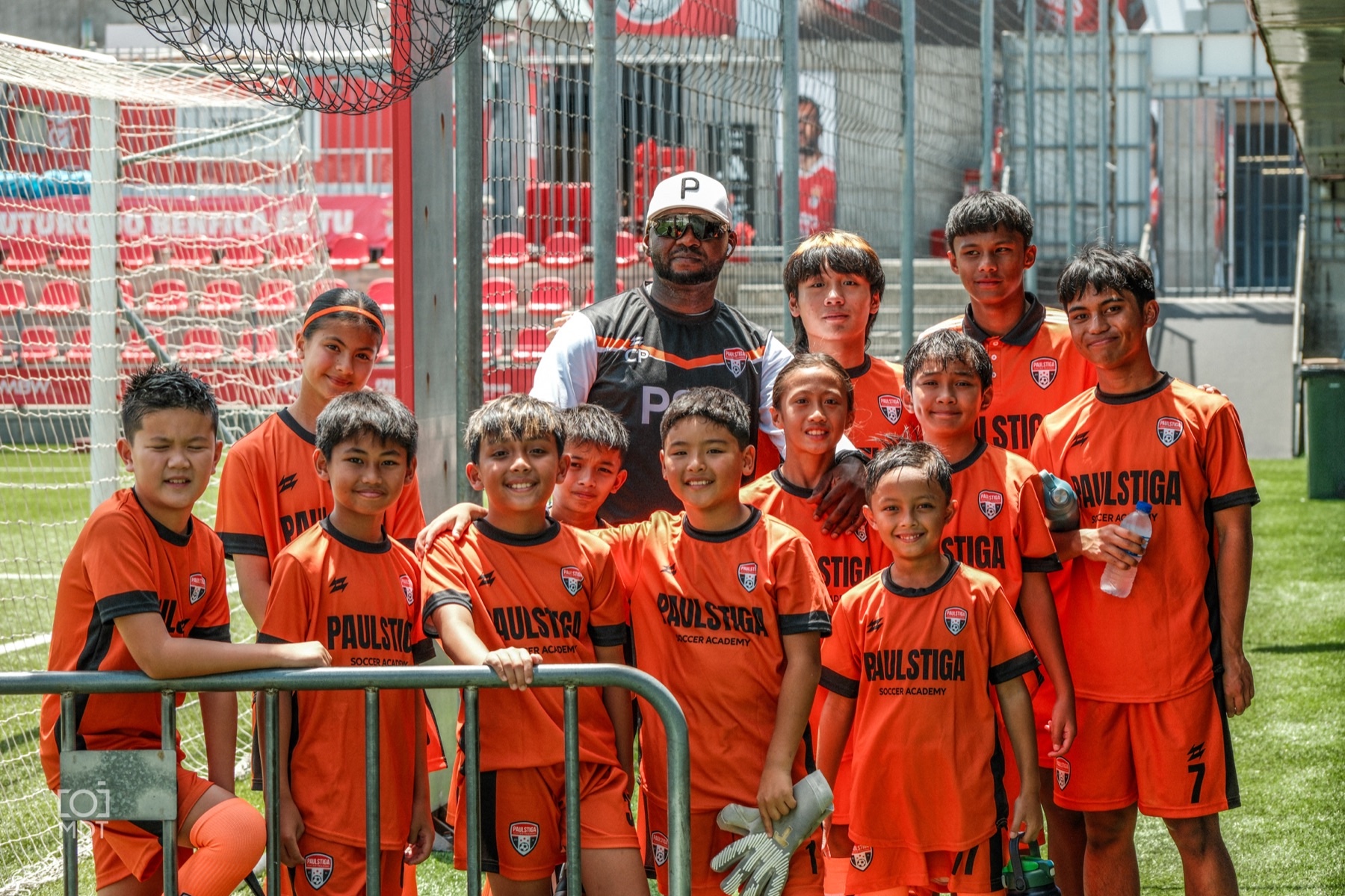 PSA players and coach posing together in orange academy kits beside a football goal
